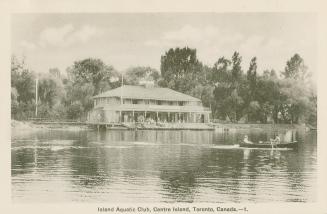 Black and white picture of people in a row boat in the water in front of a two story club house ...