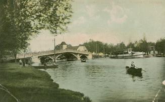 Colorized photograph of a wooden bridge over a lagoon. Person in a row boat in the foreground.