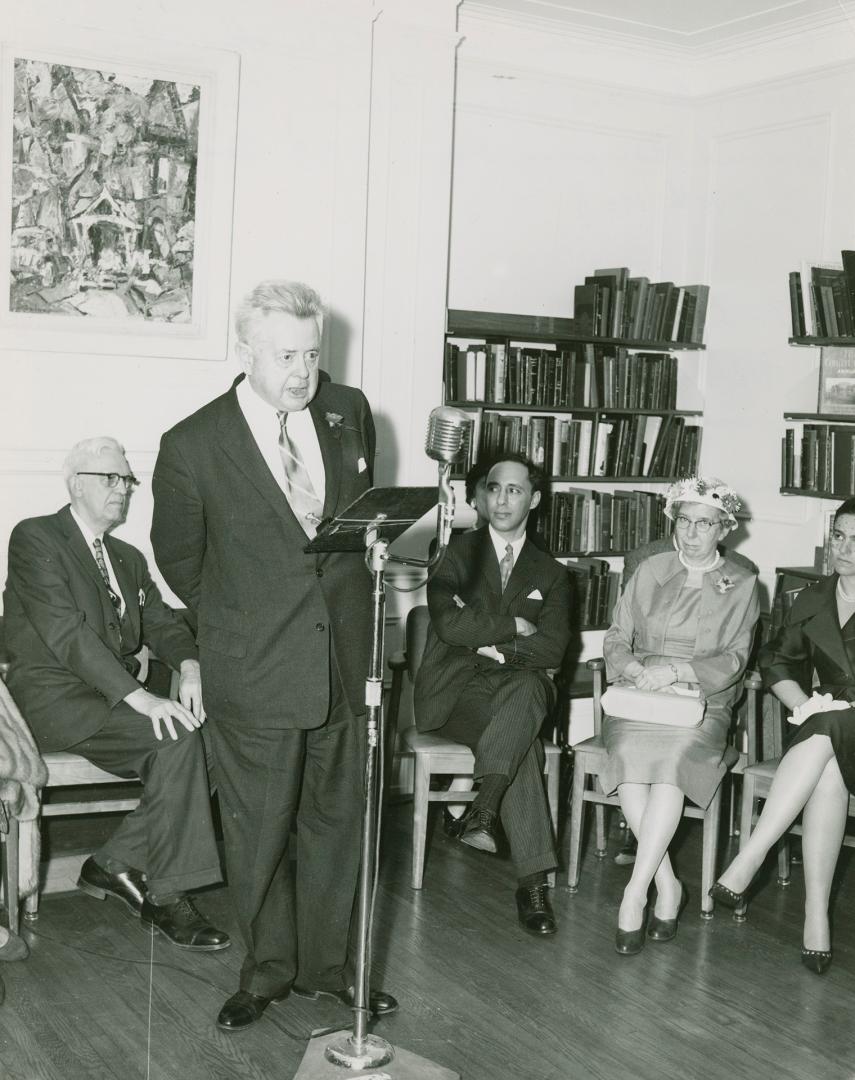 Sir Ernest MacMillan standing and speaking into a microphone with four other people sitting lis ...