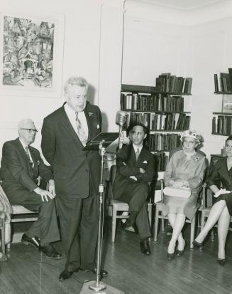 Sir Ernest MacMillan standing and speaking into a microphone with four other people sitting lis ...