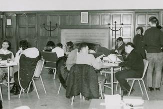 Black and white picture of tables with students sitting and studying in a library room with woo ...