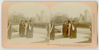 Four men in university robes standing on a walkway.