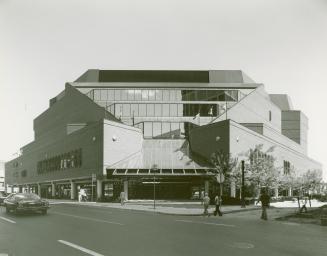Picture of the exterior of large public library building showing street and car driving past. 