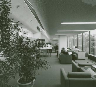 Reading area in the Metropolitan Toronto Library with lounge chairs facing large windows and ta ...