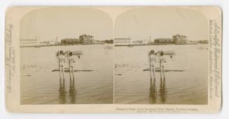 Pictures show two naked small boys watching a boat on the water with buildings on the far side.