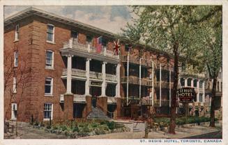 Colorized photograph of a four story, red brick hotel building with white balconies.