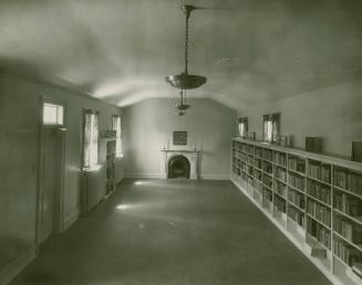 Photo of library theatre room with full bookshelves on the right hand wall and fireplace at the…