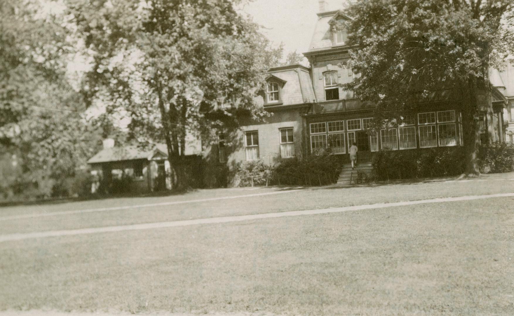 Photo taken from some distance with large lawn in front and large Victorian House surrounded by…