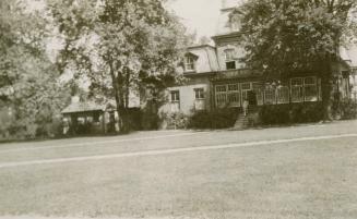 Photo taken from some distance with large lawn in front and large Victorian House surrounded by…