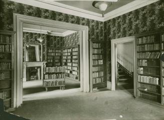 Photo of interior view of room with bookshelves lining the walls and patterned wallpaper on the…