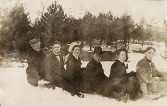 Black and white photograph of six people sitting on a toboggan.