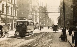 Black and white photograph of a busy downtown street with street cars, pedestrians and horse dr ...