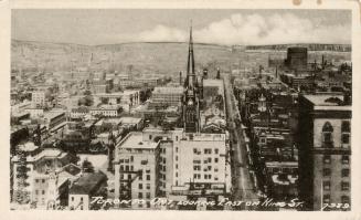 Black and white aerial view of a large city. Church spire in the center of the picture.
