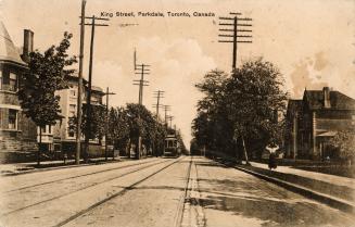 Sepia toned picture of a streetcar and tracks on a street with houses on both sides.
