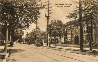 Sepia toned photograph of a city street with buildings to the right, a car driving on the stree ...