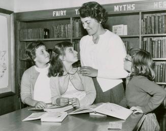 Photo of woman with three girls standing at a table with books on it. 