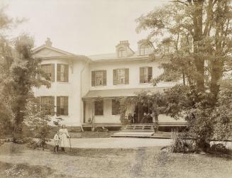 A cloudy picture of a two-storey house. A family group poses formally on chairs in the entryway ...