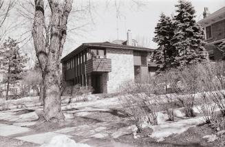 Photo of a modern two-storey brick house built on a hill, in a treed lot. Next to a driveway, t ...