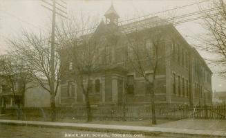 Black and white photograph of a two story school building with a covered front door at the cent…
