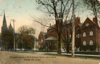 Colorized photograph of a gothic church and a Victorian school building on a tree lined street.…
