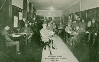 Black and white photograph of men in uniforms sitting at desk writing.