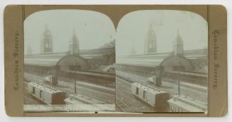 Pictures show train cars on railway tracks in front of a long building with three towers.