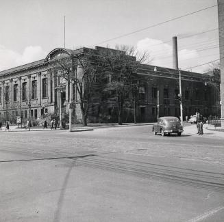 Picture of street corner with library building on the corner and car on the street.
