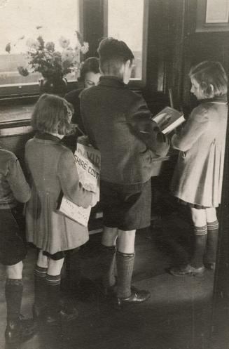 Children line up at a desk in a library to check out books.
