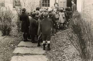 Picture of children lined up on a path waiting to get into the door of the library.
