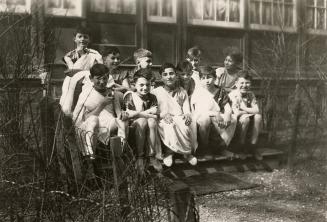 Picture of a group of boys and an adult dressed up for a play and sitting on the steps of the l ...