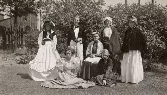 A group of seven children dressed up for a play posed outside on the lawn.
