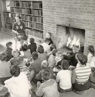 Picture of a group of children siting on the floor of a library in front of a blazing fire list ...