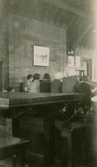 Picture of a librarian reading to a group of children in front of large brick wall with only ba ...