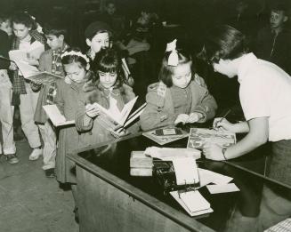 Picture of children lined up at a desk checking out books with the librarian. 