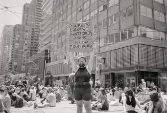 A photograph of a young adult standing on a street and holding up a sign reading "YOU'RE S…