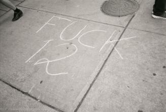 A photograph of a message reading &quot;FUCK 12&quot; written in chalk on a road. A maintenance ...