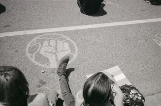 A photograph of a chalk illustration of a clenched first within a circle, drawn on a paved road ...