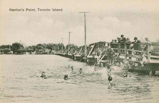 Picture of children swimming in a lake off of a long wooden boardwalk with adults looking on. 