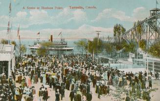 Picture of a large crowd of people at an amusement park with roller coaster and a ferry in the  ...