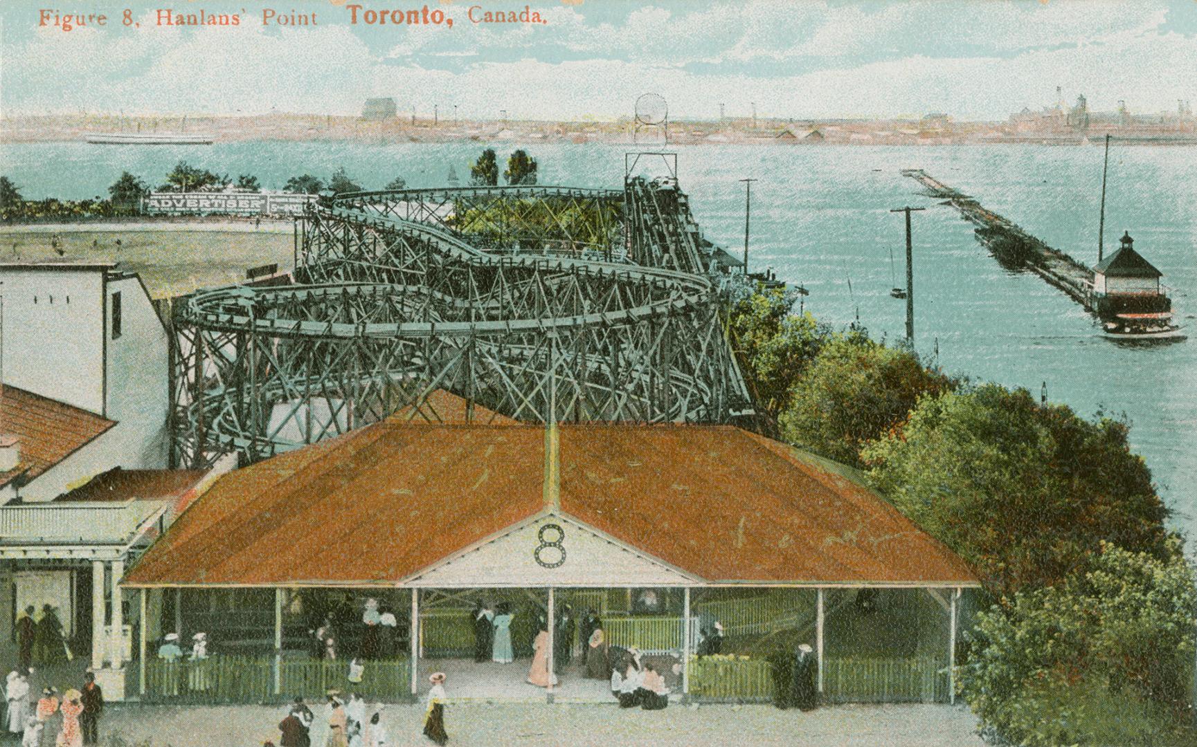 Picture of roller coaster and entrance building with people lined up and lake in the background…