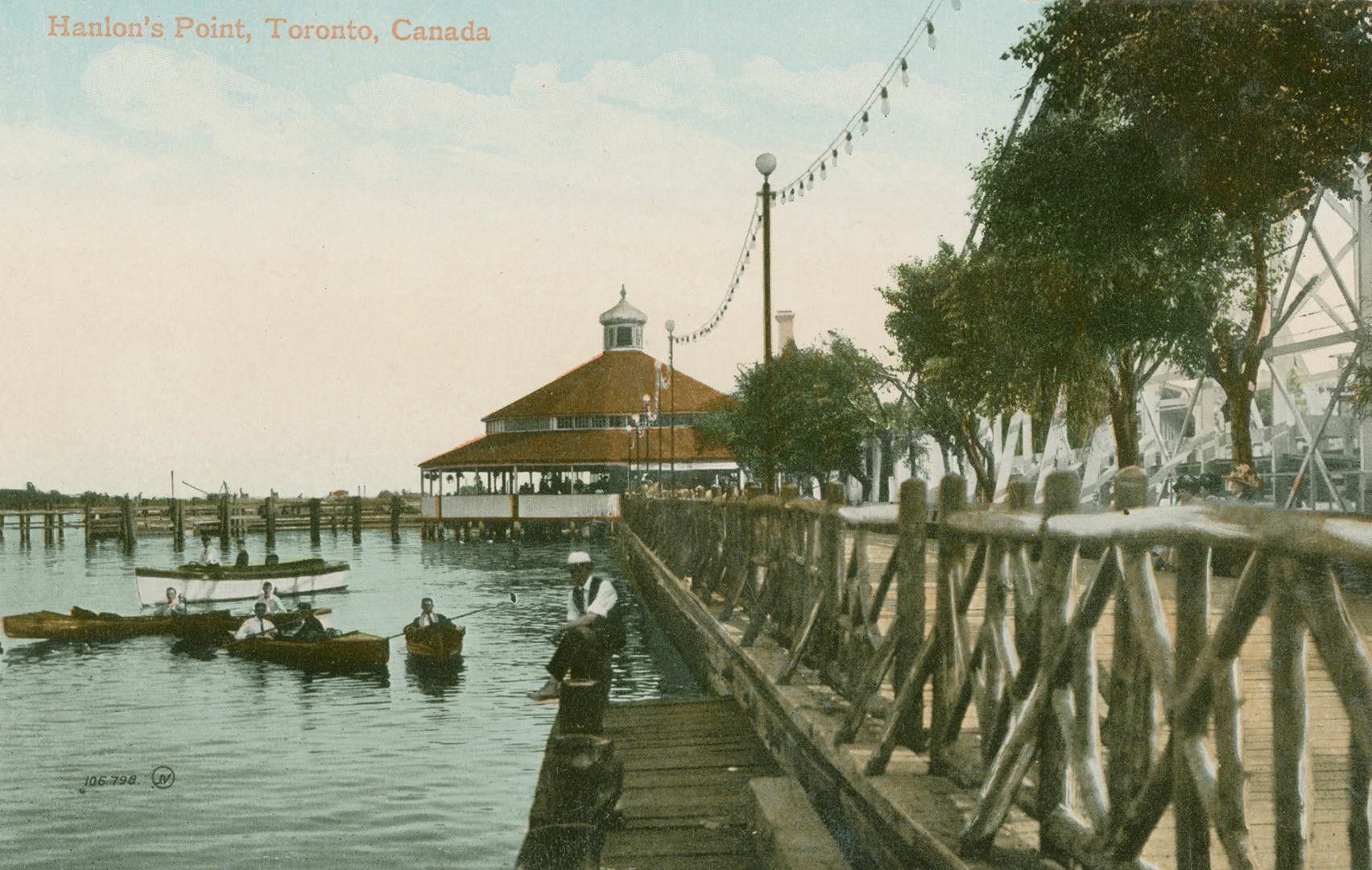 Picture of boardwalk on the right with amusement park building at the end and lake and boaters  ...