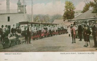 Picture of a miniature railway with people on the train and lined up to board. 