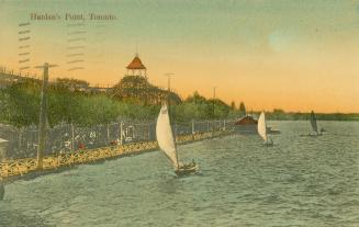 Picture of an amusement park on the lake with sailboats on the water. 