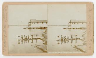 Pictures show seven children sitting in a boat on a shoreline in front of a boathouse.