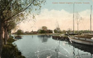 Picture of a wide lagoon with boats lining the right shore and trees on the left. 