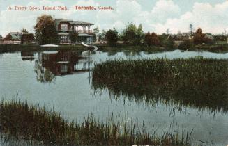 Picture of a lagoon with grasses and a house and other buildings in the background. 