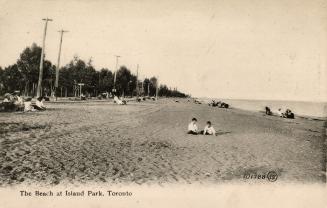 Picture of two children on a wide beach with other people in the background, trees and telephon ...