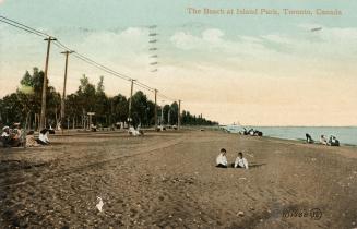 Picture of two children on a wide beach with other people in the background, trees and telephon ...