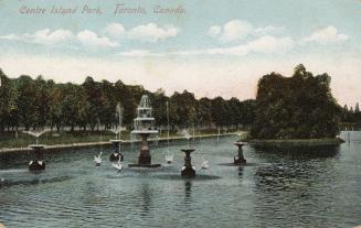 Picture of several fountains in the middle of a small lake with trees in the background.