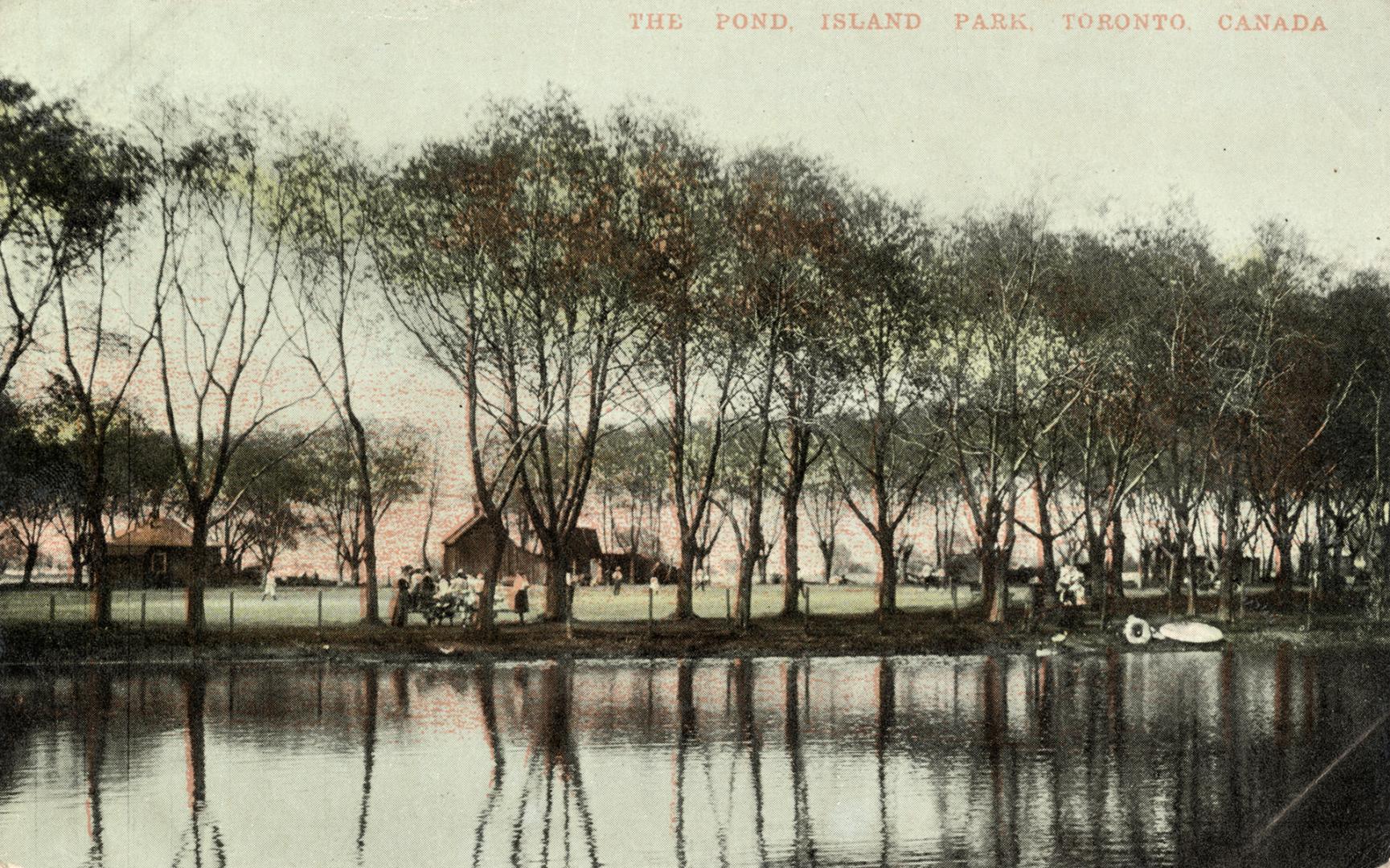 View of trees and buildings and people reflected in a large pond. 